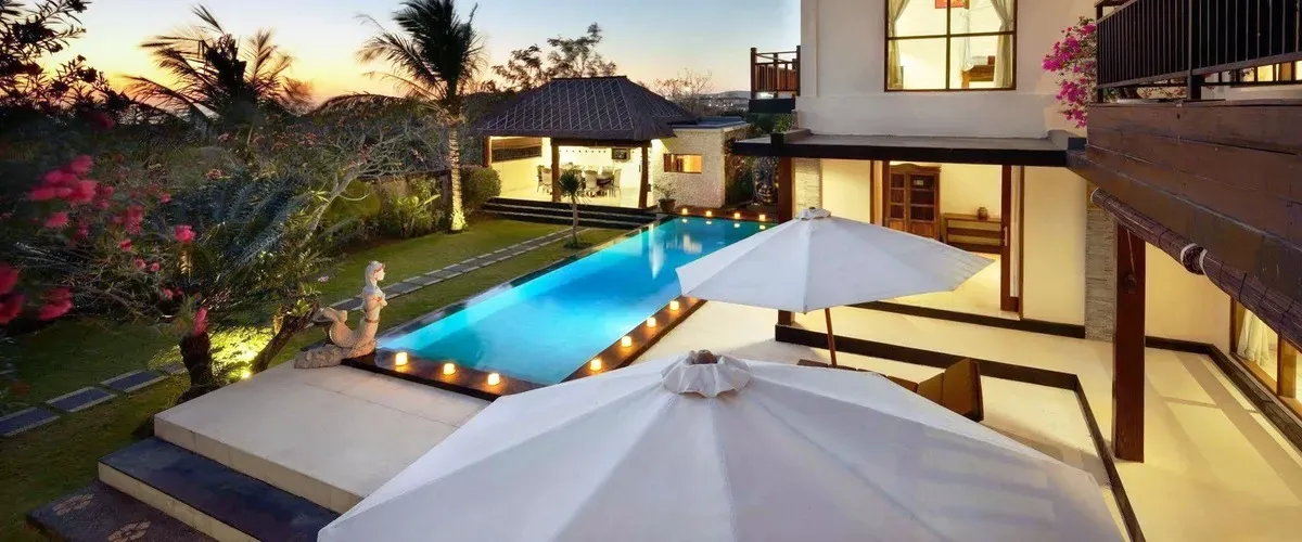 Villa at dusk with illuminated private pool and garden umbrellas